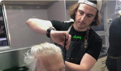 A barber cutting a client's hair inside the Barber and Connection Van
